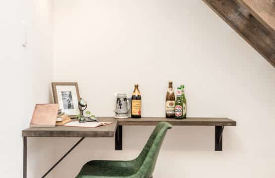 L型の木製のカウンターに、アンティークの瓶やポットが並べられ、グリーンのチェアがある、階段下ワークスペースです。