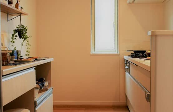 木目調の床に、ホワイトのキッチンと、同色の作業台が向かい合わせで配置されたキッチンスペースです。