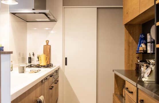 黒色の取っ手の木目調のキッチンとキッチン収納が向かい合わせで配置されたキッチンスペースです。