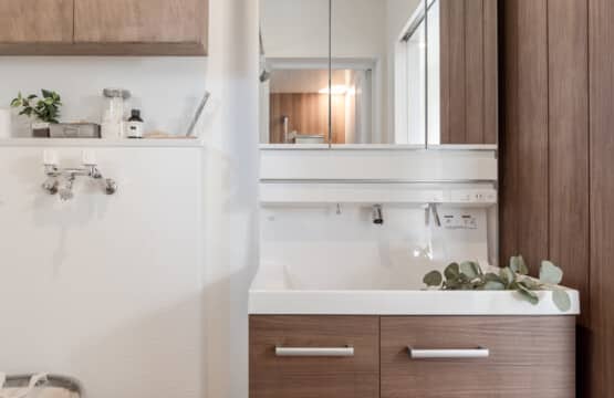 ホワイトの木目調の洗面化粧台の左横には、洗濯機置き場と、上に木製の収納棚が配置された洗面化粧室です。