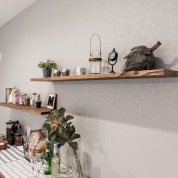 グレー調の壁に木製の飾り棚が二段あり、植物や小物類が並べられたキッチンの飾り棚です。