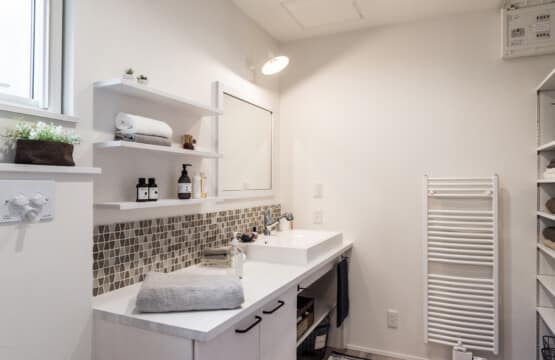 一面ホワイトの壁に、白磁の洗面台、タイルが施され、鏡の横にはタオルなどが置ける飾り棚があり、中央には物干しがあり、右手には収納棚がある洗面化粧室です。