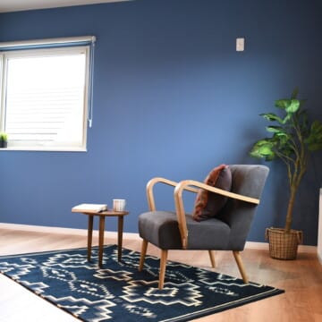 木目調の床にブルーの壁紙、北欧テイストのブルーのラグの上に、一人掛ソファとサイドテーブルが置かれた主寝室です。
