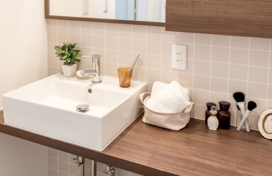 木目調の板とミラー、椅子があり、白磁の洗面台、その下は水道管が見えるようにしつらえた洗面化粧台です。