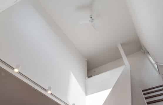 ホワイトの壁にスポットライトがついており、一階を照らし、天井にはシーリングファンがついた２階につづく吹抜けです。