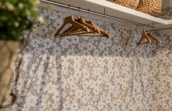 レトロな花柄の壁紙が貼られており、ホワイトの枕棚の上に籐製のカゴが並べられ、棚下のステンパイプにハンガーが掛けられたウォークインクローゼットです。