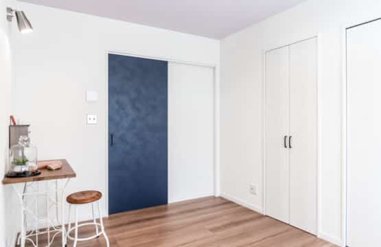 白い壁の室内で、入口のブルーのドアがアクセントになり、スポットライトが机と椅子をテラス洋室です。