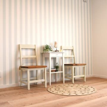 木目調の床に薄いブルーのストライプ柄の壁紙、壁にはナチュラルテイストの木の椅子とサイドテーブルが置かれた洋室2です。