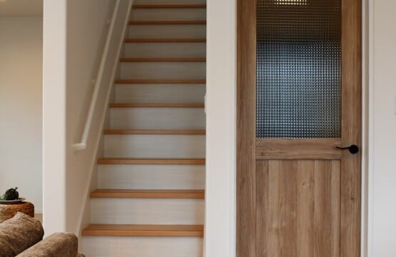 木目調の床のリビングに、北欧ナチュラルテイストの半面ガラスが付いたドア、その横には階段がある、リビング+階段です。