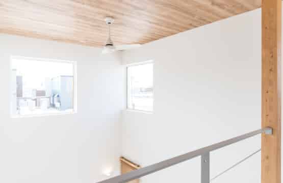 木目調の天井に白色のシーリングファンが回っており、グレー色のアイアン手摺り、大きな窓が2つある吹抜けです。
