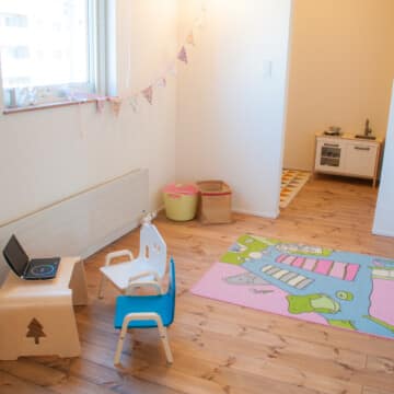 2階の洋室には子供用の木製テーブルと青と白の椅子が設えられています。その奥には子供用のキッチンが置かれています。