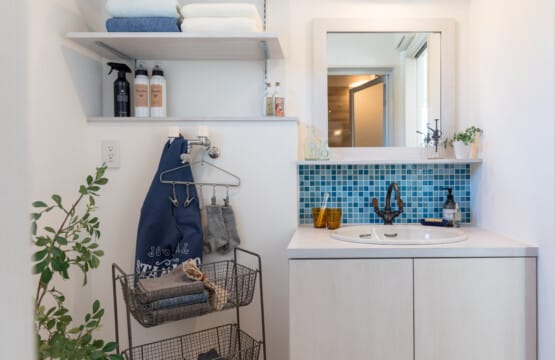 洗面化粧室にはタオルや洗剤を置いておける可動棚、水色のタイルが貼られた白色ベースの洗面化粧台があります。