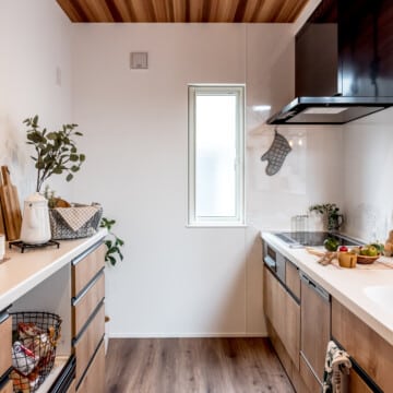 レッドシダー調クロスの天井、黒色ライン取っ手の木目調のキッチンと同柄のキッチン収納が向かい合わせで配置されたキッチンスペースです。