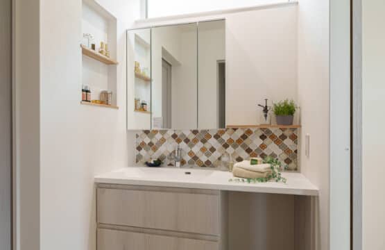 ホワイトの木目調の洗面化粧台に、コラベル柄のタイルが施され、左手側壁には2段のニッチ収納があり、床はカラフルなタイル調のクッションフロアの洗面化粧室です。