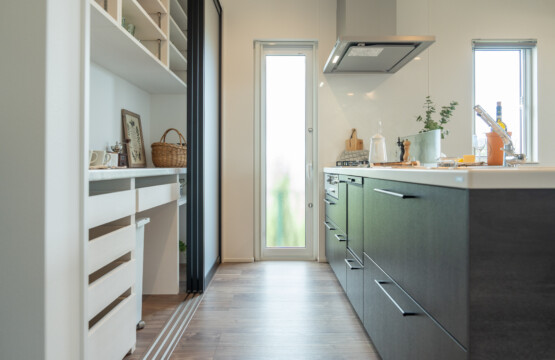 ダークグレーの木目調キッチンと、造作の白いキッチン収納が向かい合わせに並んだキッチンスペースです。