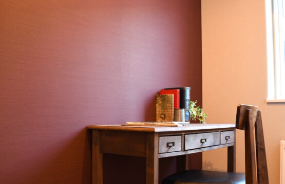 赤茶色(エンジ色)の壁紙にナチュラルモダンなデスクと椅子があり、アンティークな本が飾られた洋室2です。