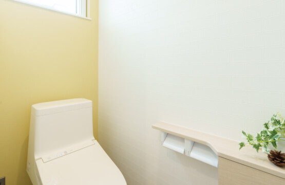 テラコッタ調の床、右側壁がレモンイエロー色、左側の壁は白色で2連の紙巻き器が付いたトイレカウンター収納が設置されているおトイレです。