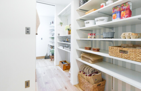 節目のあるナラ樫のフローリング、白い棚板の可動棚に食器や食品のストックが並んでいて、 棚の背面の壁は、縦ストライプのアクセントクロスが貼られているパントリーです。